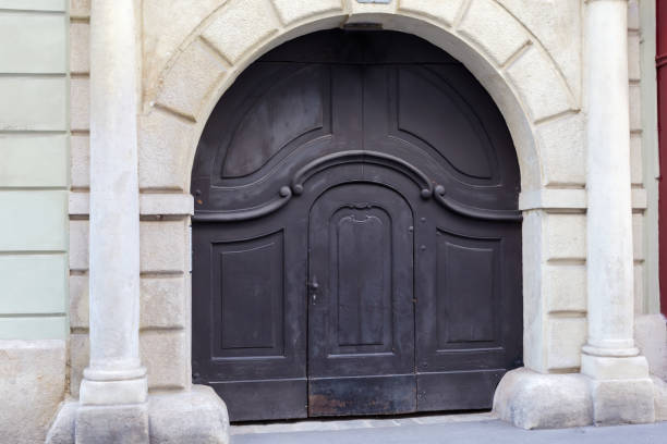istock Old wooden gate painted black with wicket in arched passage 2184003054