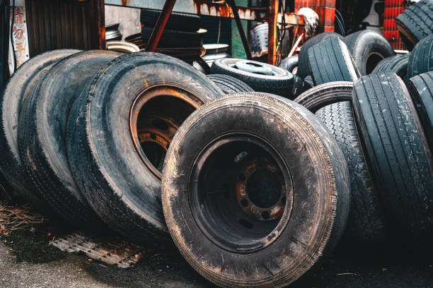 A collection of worn-out and discarded tires stacked together, showcasing varying textures, treads, and weathered surfaces. The close-up perspective emphasizes the rugged details and the layered arrangement, hinting at the end of their functional life.
