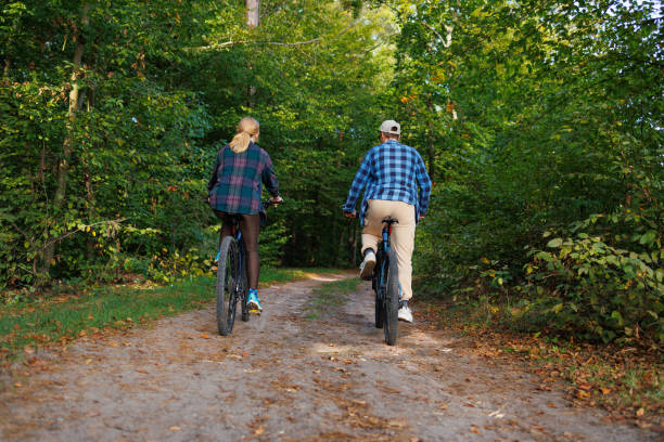 istock Young man and woman ride a bicycle through a forest area, back view 2184024696