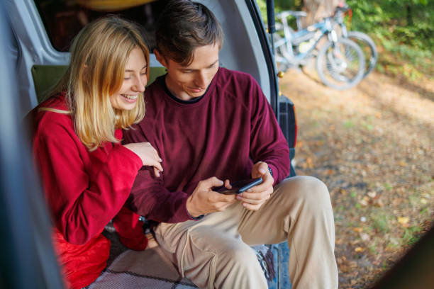 istock Cute couple watching something interesting on a smartphone while sitting in their homemade camping van in the forest 2184025924