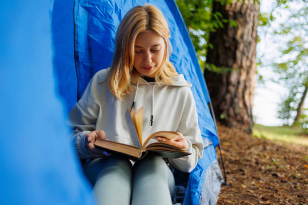 istock Young woman leafing through a book while sitting in a tent surrounded by nature 2184026001