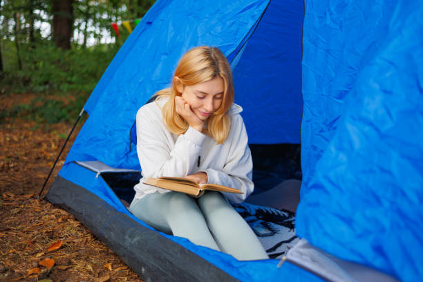 istock A young woman reads a book with interest while sitting in a camping tent 2184026144