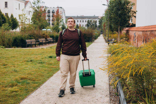 istock Happy 30s man pulling green suitcase outdoors. Rear view. Copy space. Man walking on the street with travel bag. Full body 2184026168