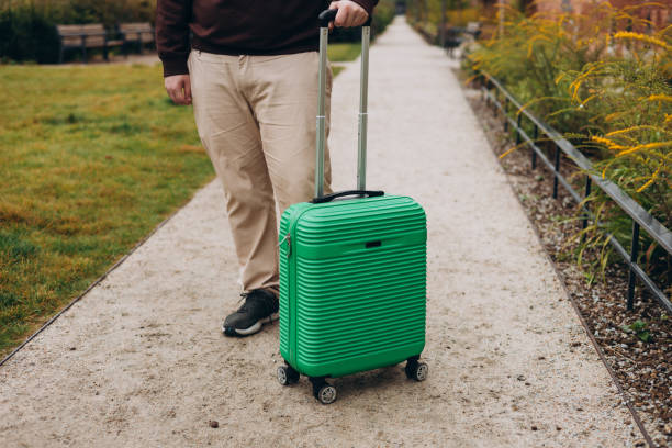 istock Unrecognizable man pulling green suitcase outdoors. Copy space. Man walking on the street with travel bag. Male dragging baggage near hotel. Travel Fashion. 2184026502