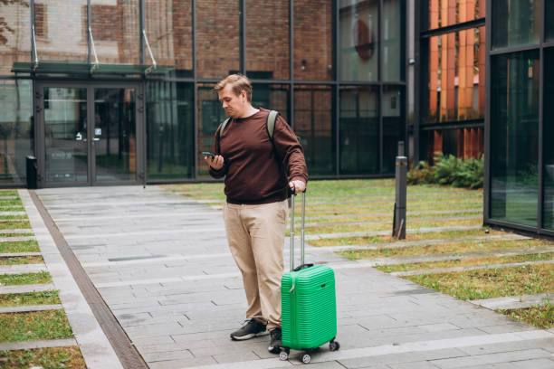 istock Upset sad, skeptical man holding smartphone gadget for communicate outdoors. Negative people emotion, Urban lifestyle concept. 30s male with green suitcase reading bad news, full body 2184026588