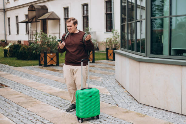 istock Upset sad, skeptical man holding smartphone gadget for communicate outdoors. Negative people emotion, Urban lifestyle concept. Angry 30s male with green suitcase reading bad news, full body 2184026668