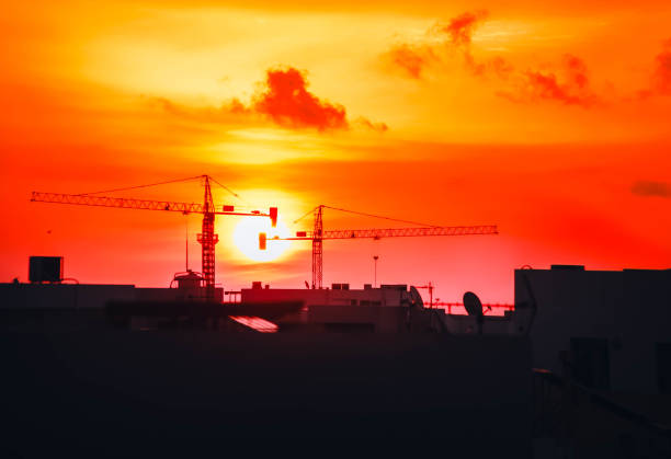 A captivating sunset view featuring silhouetted construction cranes against a vibrant orange and red sky. This powerful industrial landscape captures the blend of urban development and natural beauty.