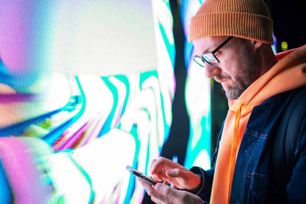 istock Mid adult man using mobile at night while standing by neon light billboard 2184036083