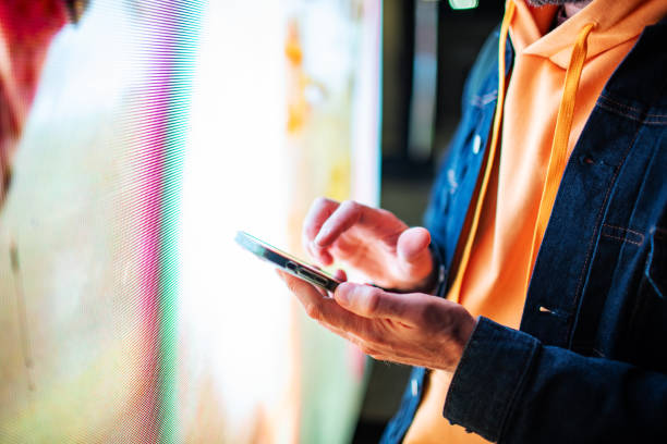 istock Closeup of mobile in hands with neon light billboard at background 2184036095
