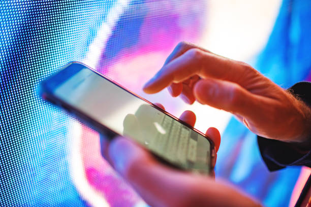 Closeup of mobile in hands with neon light billboard at background