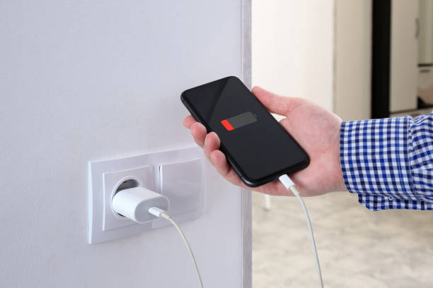 istock A man holds a smartphone in his hand, connected cable to a charger from electrical socket. Against the background of a residential apartment. 2184041658