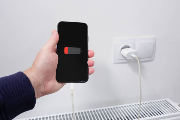 istock A man holds a smartphone in his hand, connected cable to a charger from electrical socket. Against the background of a residential apartment. 2184041873
