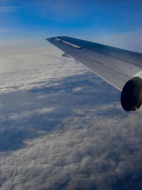 An airplane wing and dense clouds beneath it against a backdrop of blue dawn sky, vertical shot, winter vacation, airplane travel, view of clouds from the airplane window.