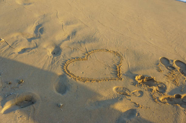 A heart shape etched in warm sand, surrounded by gentle footprints on a serene beach at dusk.