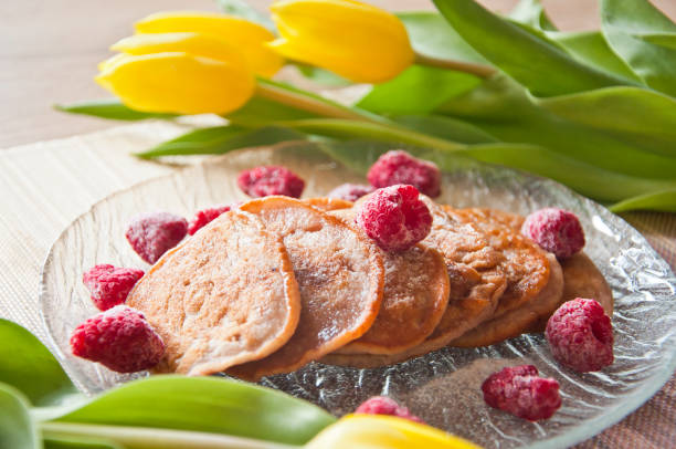 Bunch of tasty homemade banana pies decorated with frozen raspberries with yellow tulips and bananas in the background