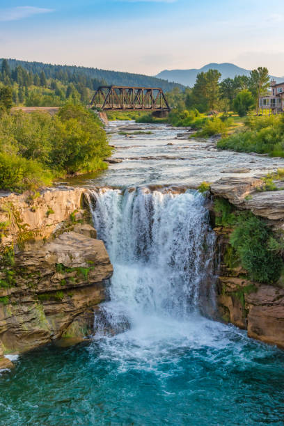istock Serene Waterfall Amidst Lush Greenery with Rustic Bridge and House 2184059012