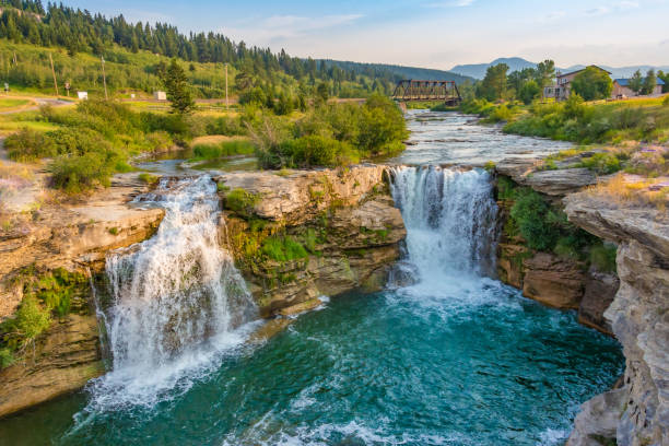 istock Serene Waterfall Amidst Lush Greenery with Rustic Bridge and House 2184059141
