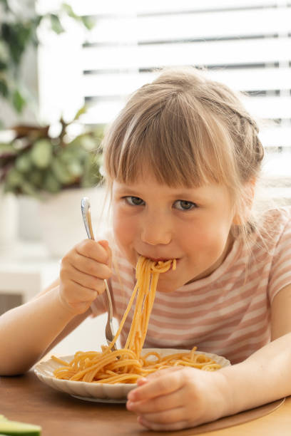 istock Happy little girl eats spaghetti sitting at kitchen table 2184063169