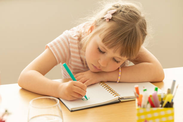 istock Cute little girl draws picture on notepad page at table 2184064457