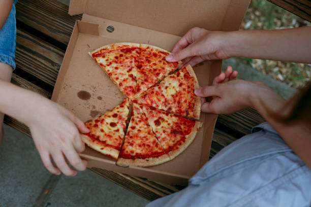 istock Friends eating pizza on a park bench. 2184071407