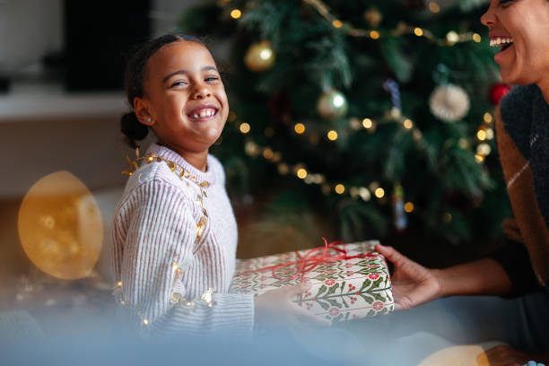istock Joyful Child Receiving Christmas Gift by Festive Tree 2184072648