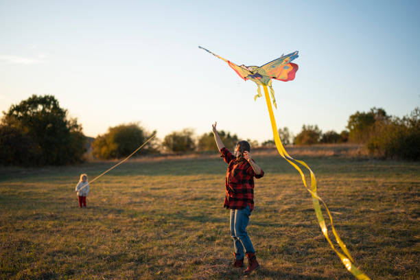 A helping hand. Caring mother teaches little girl to fly a kite in autumn nature at sunset. Child development, learning, freedom, joy, & connecting with nature.