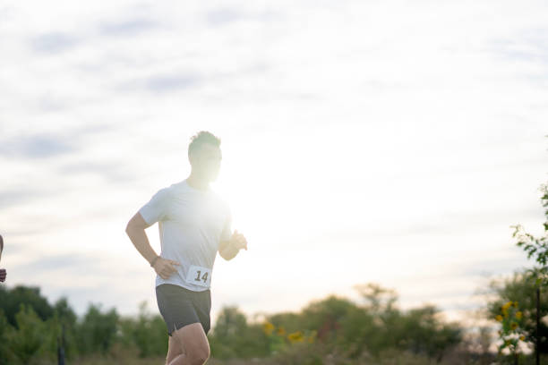 A male adult is seen running outside as he participates in a race.  He is dressed comfortably and has a race bib number on as he focuses on his breathing.