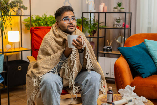 istock Sick Indian man wrapped in plaid sit alone shivering trembling from cold on chair drinking hot tea 2184076406