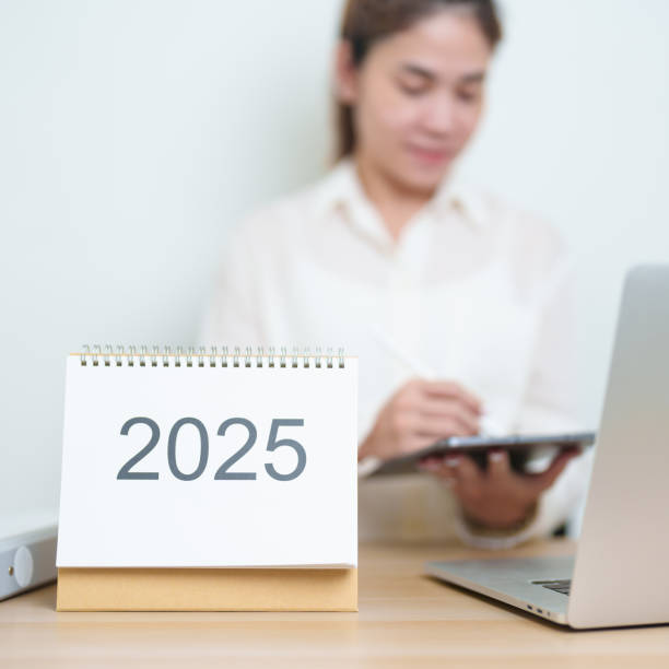 istock 2025 Year Calendar on table with business woman using laptop computer, working and writing in office. countdown, Happy New Year, Resolution, Year End and New Start and Goals Plan Action Concept 2184082697