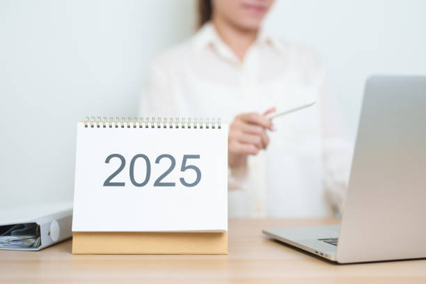 istock 2025 Year Calendar on table with business woman using laptop computer, working and writing in office. countdown, Happy New Year, Resolution, Year End and New Start and Goals Plan Action Concept 2184082700