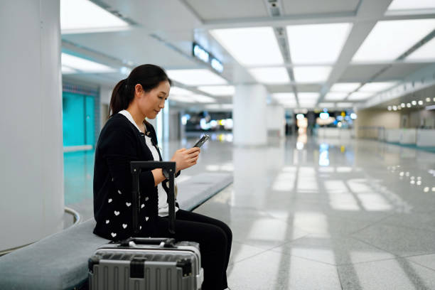 istock Woman with Luggage at Airport Using Smartphone While Waiting 2184087931