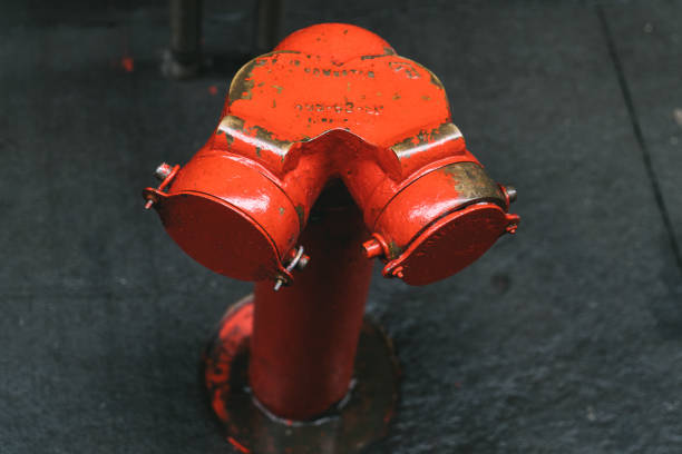 A detailed closeup view of a vibrant red fire hydrant firmly attached to a textured and gritty asphalt surface