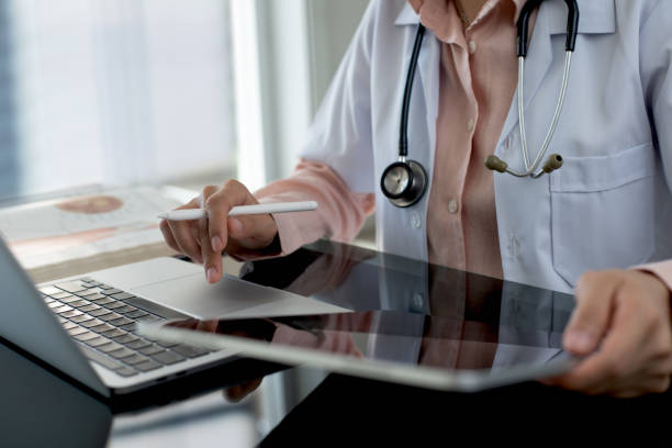 istock Female doctor working on laptop computer searching the information and using digital tablet at doctor's office. Medical student using computer, healthcare and medicine concept 2184095172