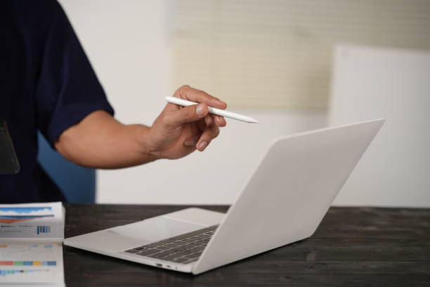 istock A focused businessman sits at his office desk, analyzing a paper chart while working on his laptop. He examines financial and marketing reports, concentrating on data for strategic decision-making. 2184099845