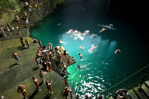 High-angle view of female traveller swith arms raised wimming in the Rangko cave with turquoise water and stalagmite formations around on Flores island, Indonesia