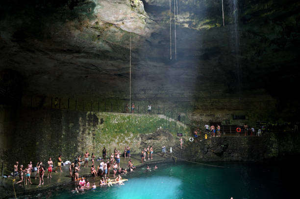Two women in swimsuits swim in a mysterious cenote with greenish water and limestone walls in an underground cave, Yucatan, Mexico