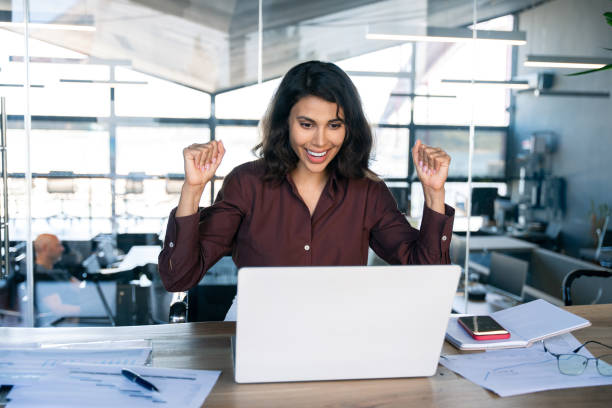 istock Happy excited young businesswoman looking at laptop pc computer screen doing yes triumph win gesture. Smiling latin hispanic business woman successful winner celebrating winning in office. Copy space 2184105574