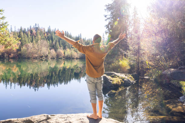 istock Man Embracing Nature with Open Arms by a Tranquil Lake 2184113127