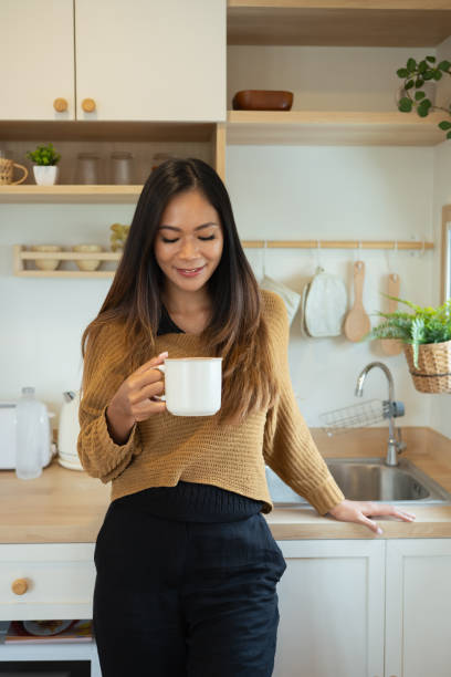 istock Smiling pretty woman enjoying a cup of coffee while sitting on kitchen counter 2184113908