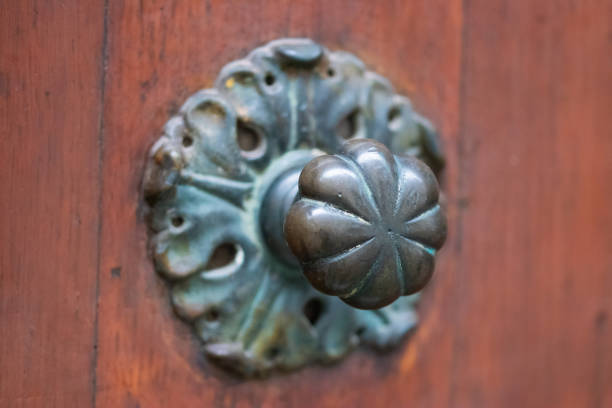 Close-up of a beautifully aged, antique door knob with intricate leaf-like detailing, set against a rustic wooden door. The tarnished metal gives it a timeless, vintage charm, perfect for themes related to history, architecture, and old-world craftsmanship. Ideal for use in home decor, design inspiration, and restoration projects.