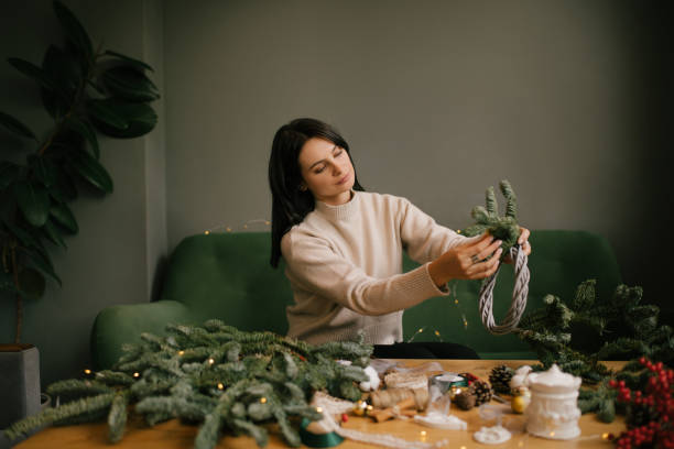 istock Woman making Christmas wreath using natural pine branches, sitting near wooden table. 2184120088
