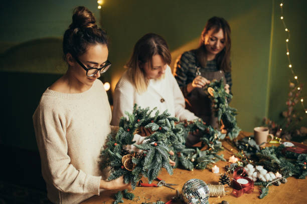 istock Happy women making Christmas wreath using natural pine branches and festive decorations. 2184120193