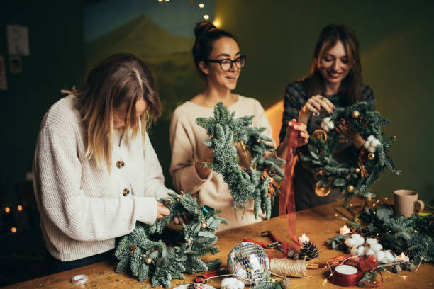 istock Happy women making Christmas wreath using natural pine branches and festive decorations. 2184120196