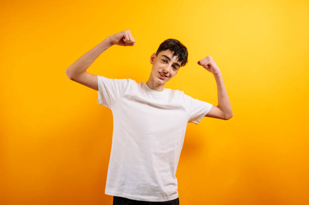 Teenager flexing arms, confident, yellow background.