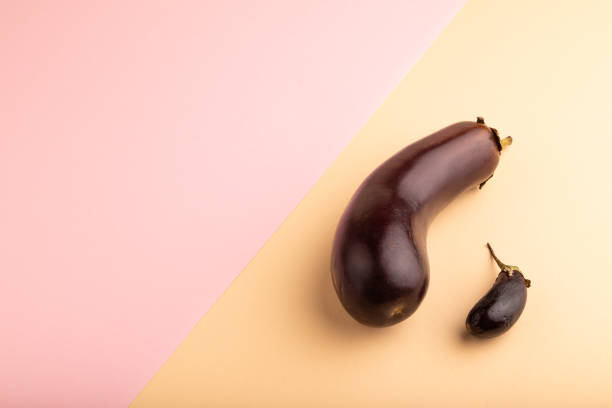 istock Two Eggplantsbig and small on pink and orange pastel paper, side view, copy space 2184125000