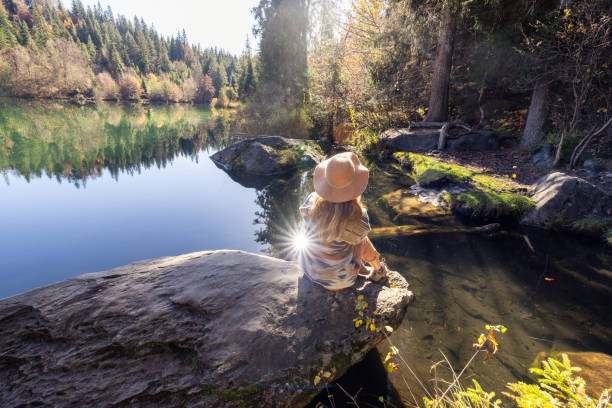 istock Woman Sitting on Rock by Tranquil Lake in Forest 2184130993