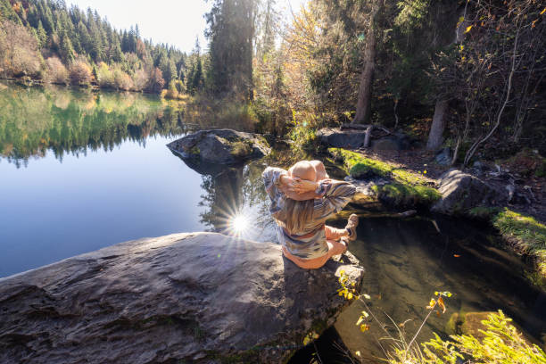 istock Woman Sitting on Rock by Tranquil Lake in Forest 2184131021
