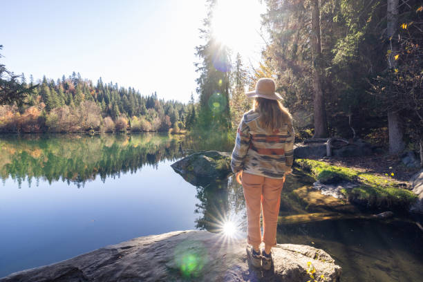 istock Woman Standing on Rock Overlooking Tranquil Lake in Sunlight 2184131027