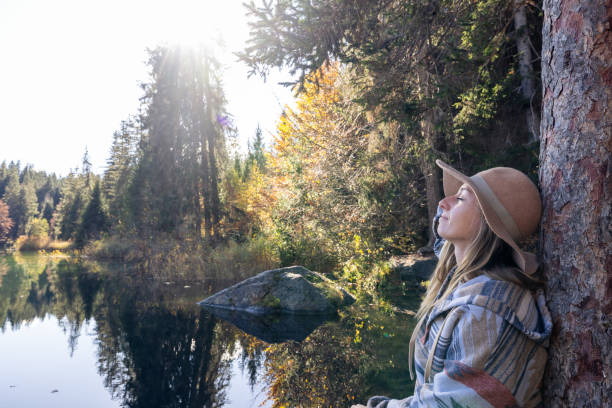 istock Woman Meditating by Lake in Sunlit Forest 2184131172