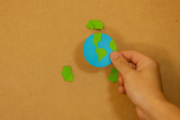 istock Hand placing a paper planet earth with recycling signal on a board 2184132268